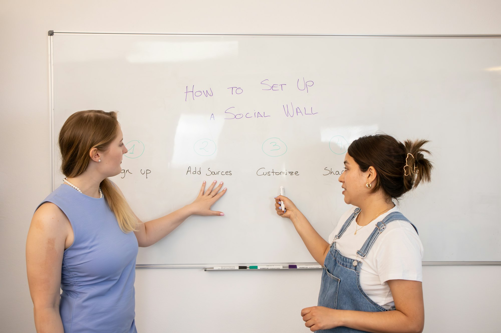 Professora e aluna conversando em inglês diante de um quadro branco
